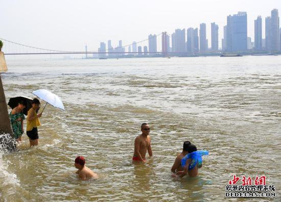 7月25日，武汉武昌江边，市民打伞遮阳站在水中降温。当日，武汉中心气象台发布高温红色预警。武汉、十堰、襄阳等9个地市高温突破40℃。未来三天，湖北省大部地区最高气温为37℃到40℃，局部地区最高气温将达到41℃到42℃。 中新社记者 张畅 摄